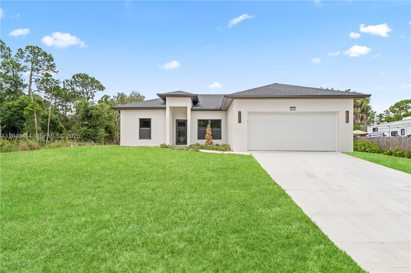 A modern, single-story white stucco house features a two-car garage and a front entrance — 2602 E 2nd st, Lehigh Acres FL 33936, LEHIGH ACRES, FL