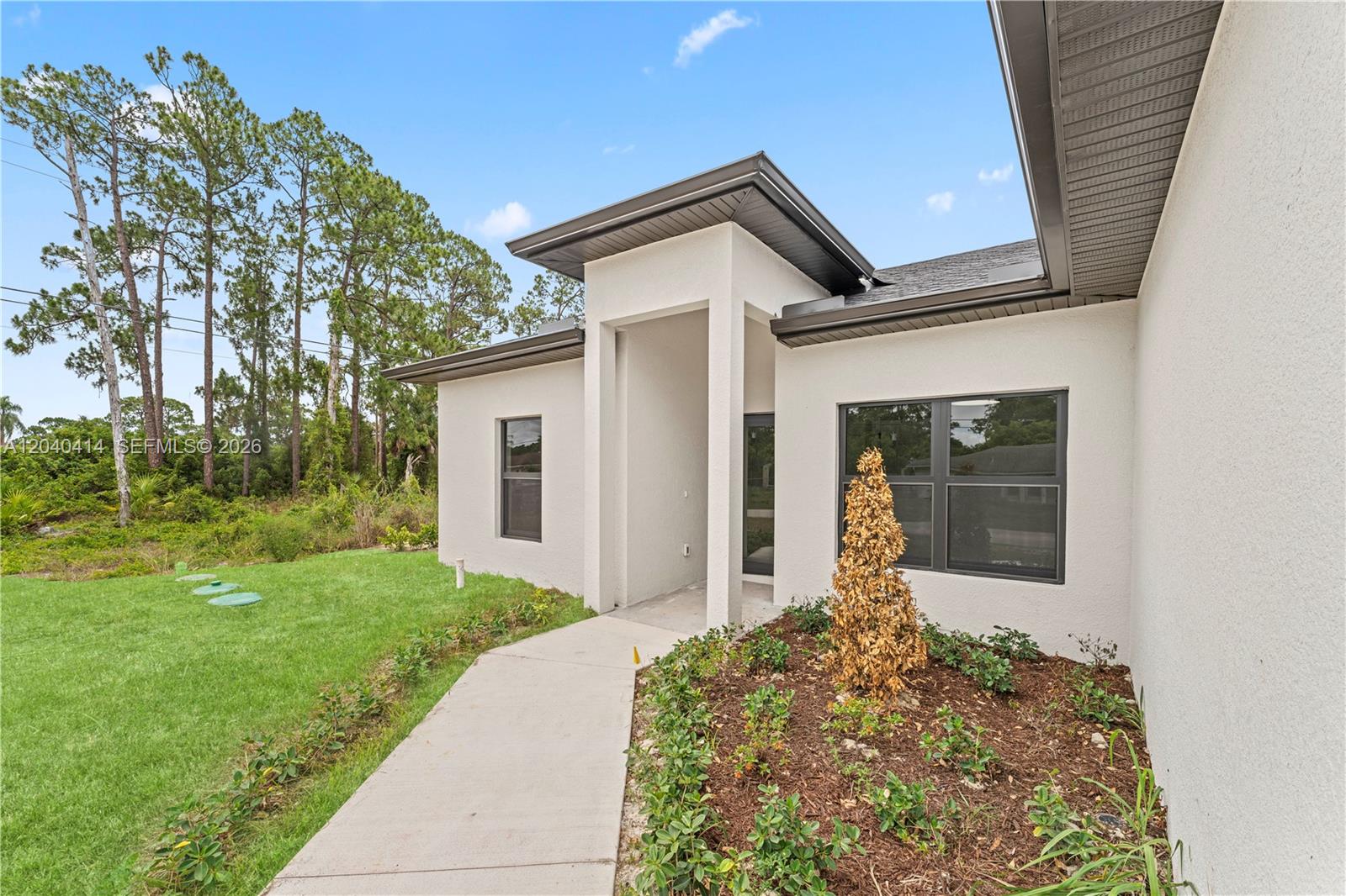 The exterior of a modern white house features a concrete walkway and a small garden — 2602 E 2nd st, Lehigh Acres FL 33936, LEHIGH ACRES, FL