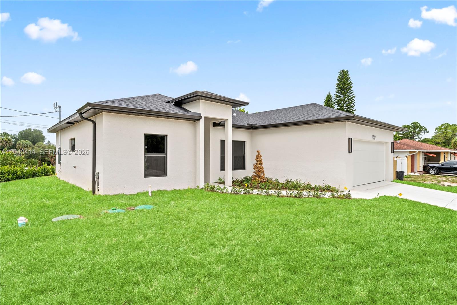 A single-story house with a white stucco exterior, dark roof, and a two-car garage — 2602 E 2nd st, Lehigh Acres FL 33936, LEHIGH ACRES, FL