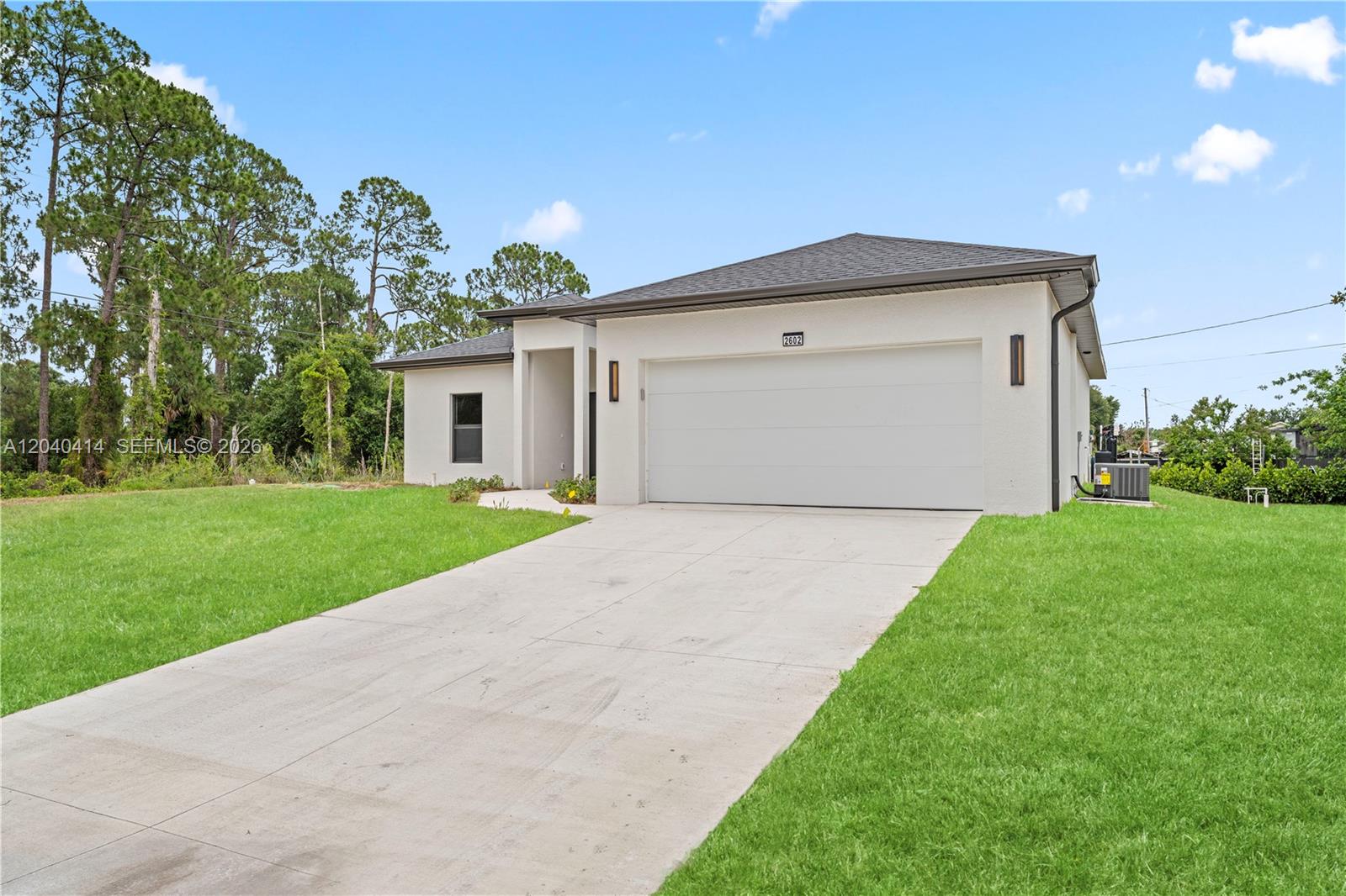 A single-story house with a white stucco exterior, a two-car garage, and a concrete driveway — 2602 E 2nd st, Lehigh Acres FL 33936, LEHIGH ACRES, FL