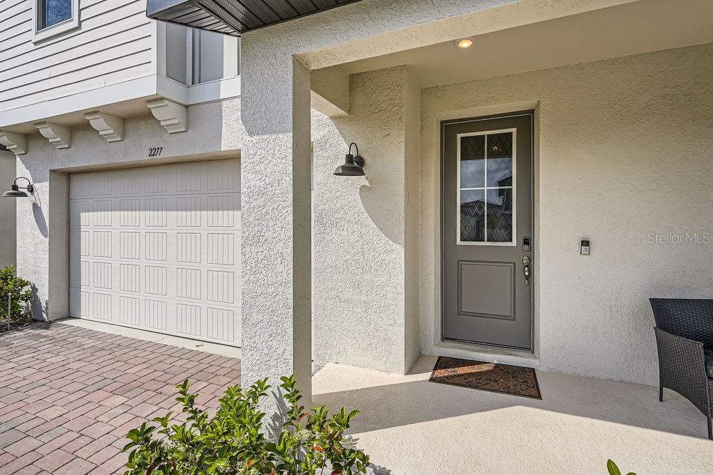 A gray front door with a glass pane sits beside a garage with a brick driveway — 2277 CROSSBOW STREET, CLERMONT, FL