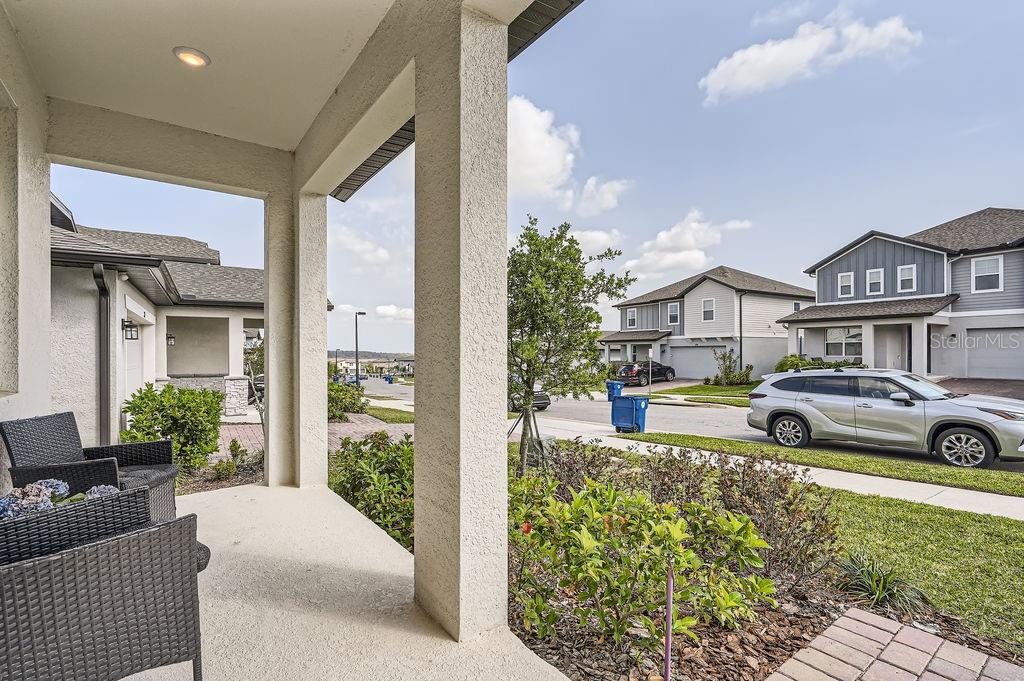 A covered front porch with wicker chairs overlooks a suburban street with houses and cars — 2277 CROSSBOW STREET, CLERMONT, FL