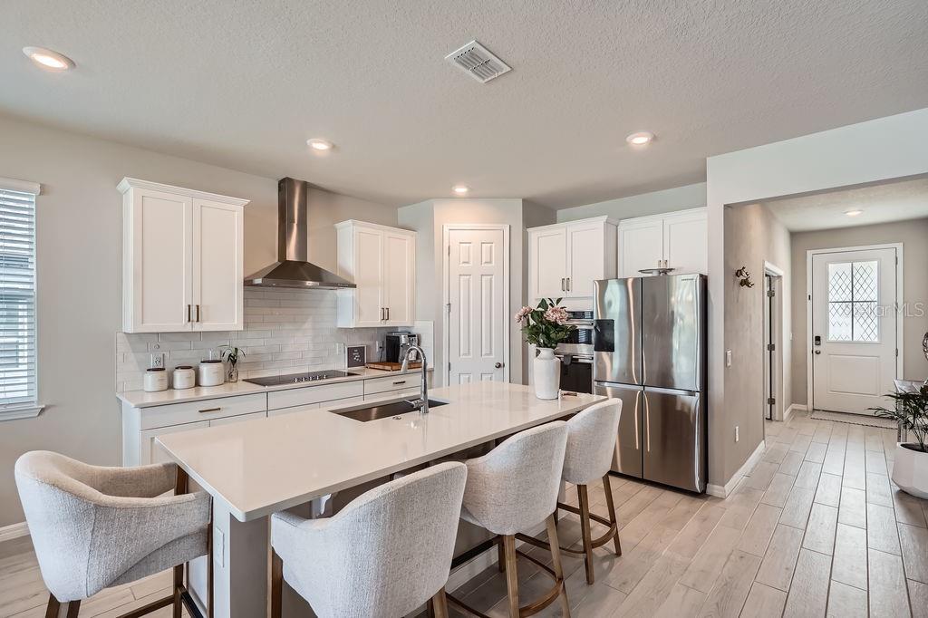 A modern kitchen features white cabinetry, a large quartz island, stainless steel appliances, and tile flooring — 2277 CROSSBOW STREET, CLERMONT, FL
