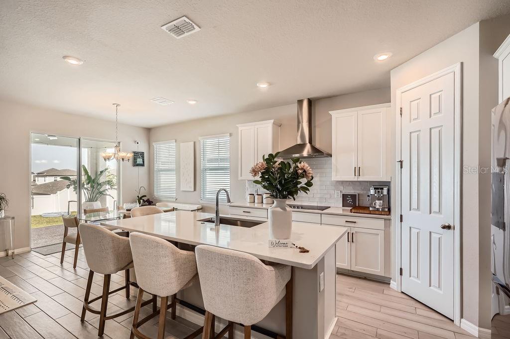 A modern kitchen features white cabinets, a quartz island with bar seating, and tile flooring — 2277 CROSSBOW STREET, CLERMONT, FL