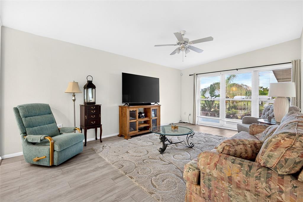 A living room features a patterned sofa, a teal recliner, a television, and wood flooring — 3349 ROCK CREEK DRIVE, PORT CHARLOTTE, FL
