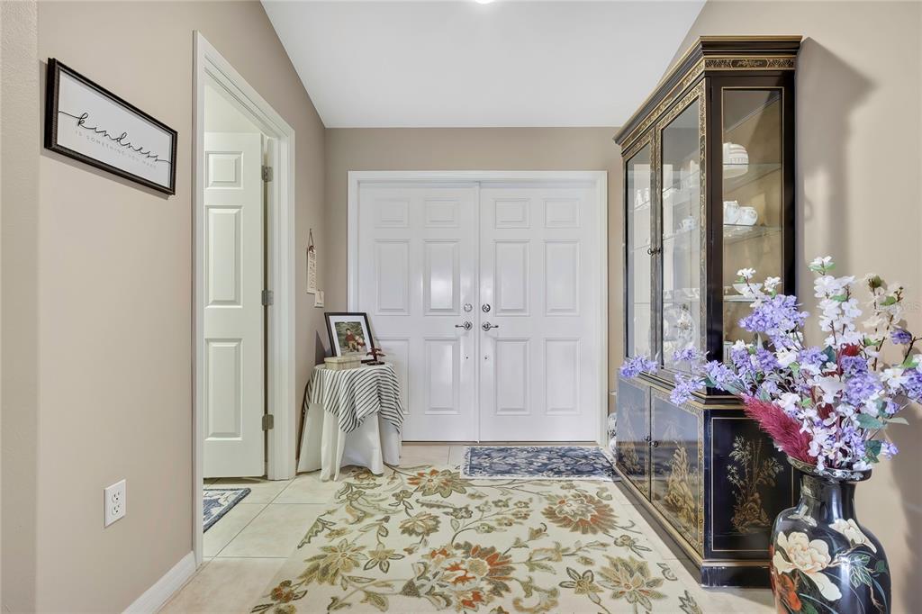 A foyer features a floral rug, a black display cabinet, and white double entry doors — 11910 HERITAGE POINT DRIVE, HUDSON, FL