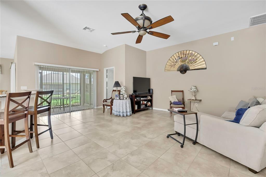 A living room with tile flooring, a ceiling fan, a television, and a sliding glass door — 11910 HERITAGE POINT DRIVE, HUDSON, FL
