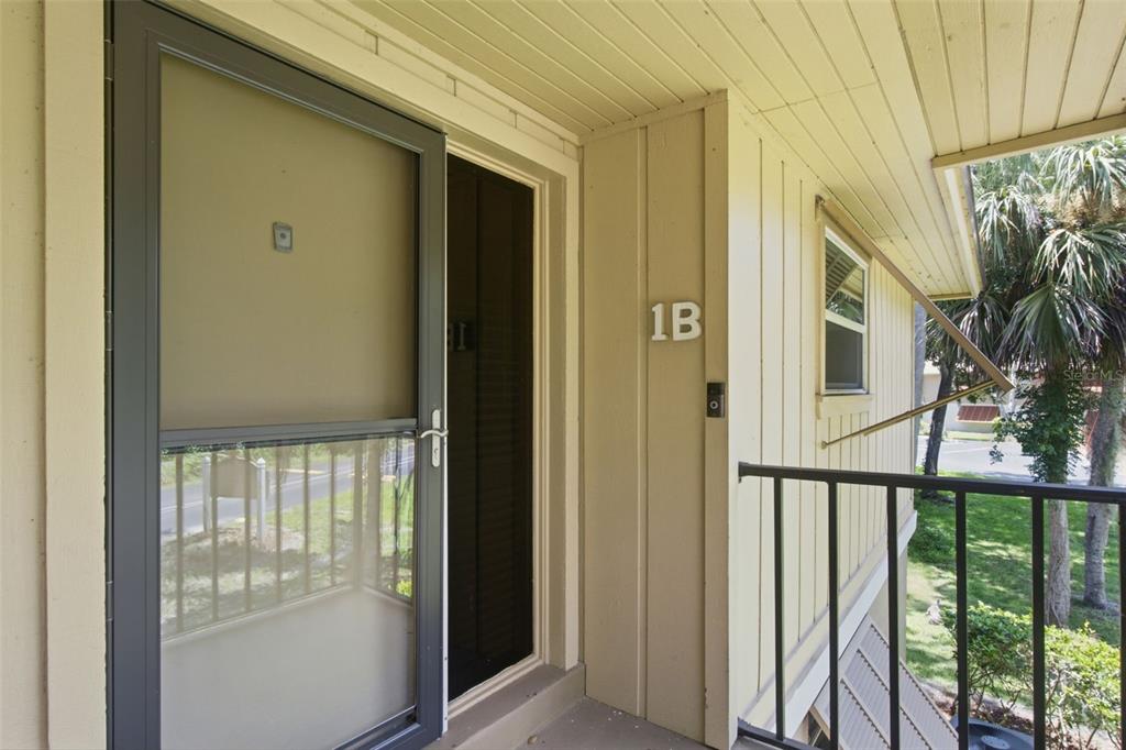 An exterior view of a residential unit entrance labeled 1B with a screen door — 140 ORCHID WOODS COURT UNIT 1B, DELTONA, FL