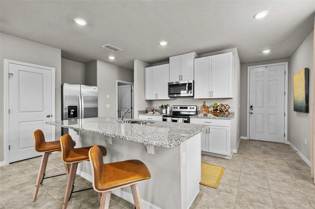 A kitchen features white cabinets, granite countertops, a stainless steel refrigerator, and three bar stools — 8683 HOLLY GROVE COURT UNIT Oakville, RIVERVIEW, FL