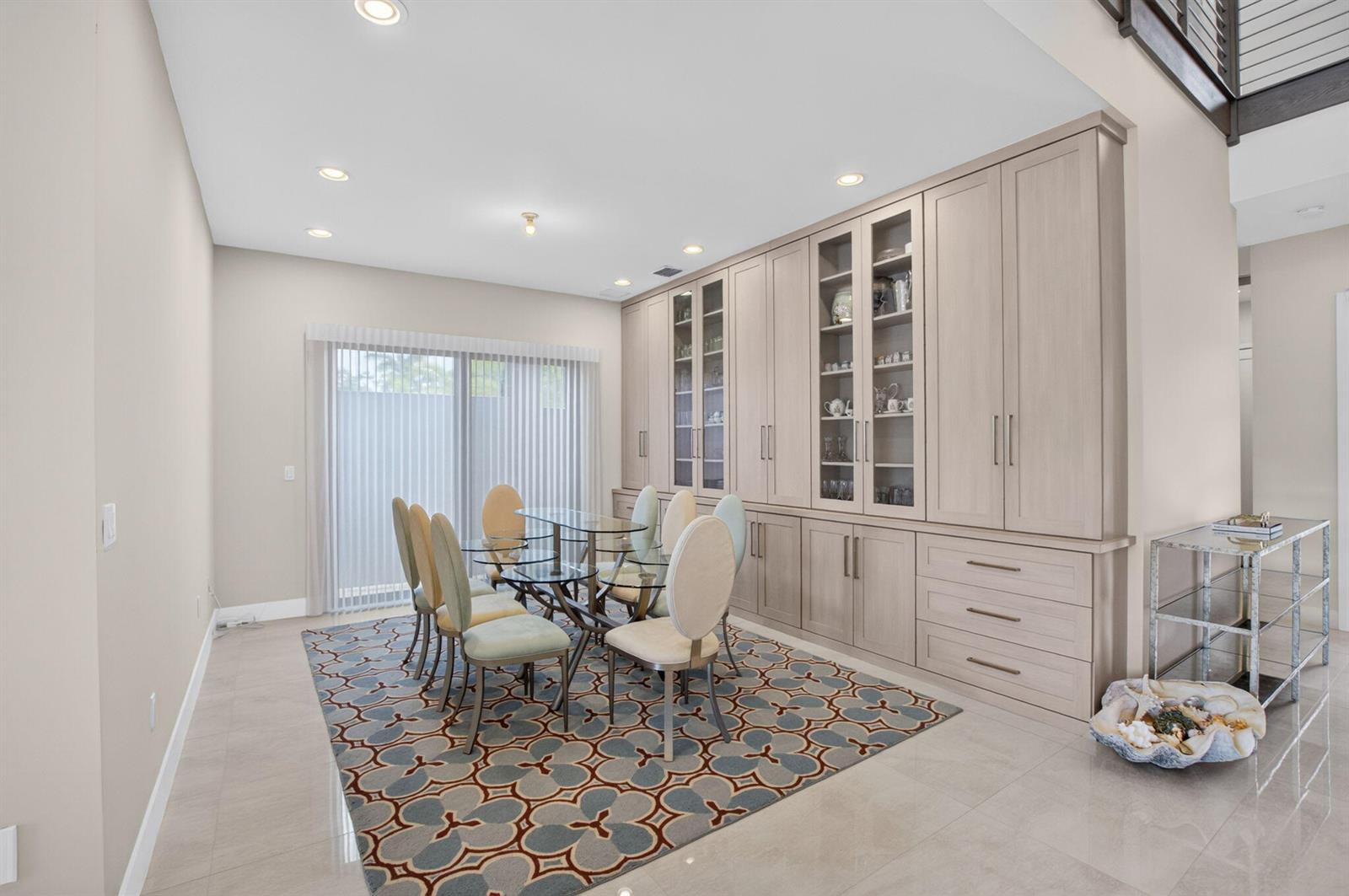 A dining room features a glass table, upholstered chairs, a patterned rug, and built-in cabinetry — 17100 Wandering Wave Avenue, Boca Raton FL 33496, BOCA RATON, FL