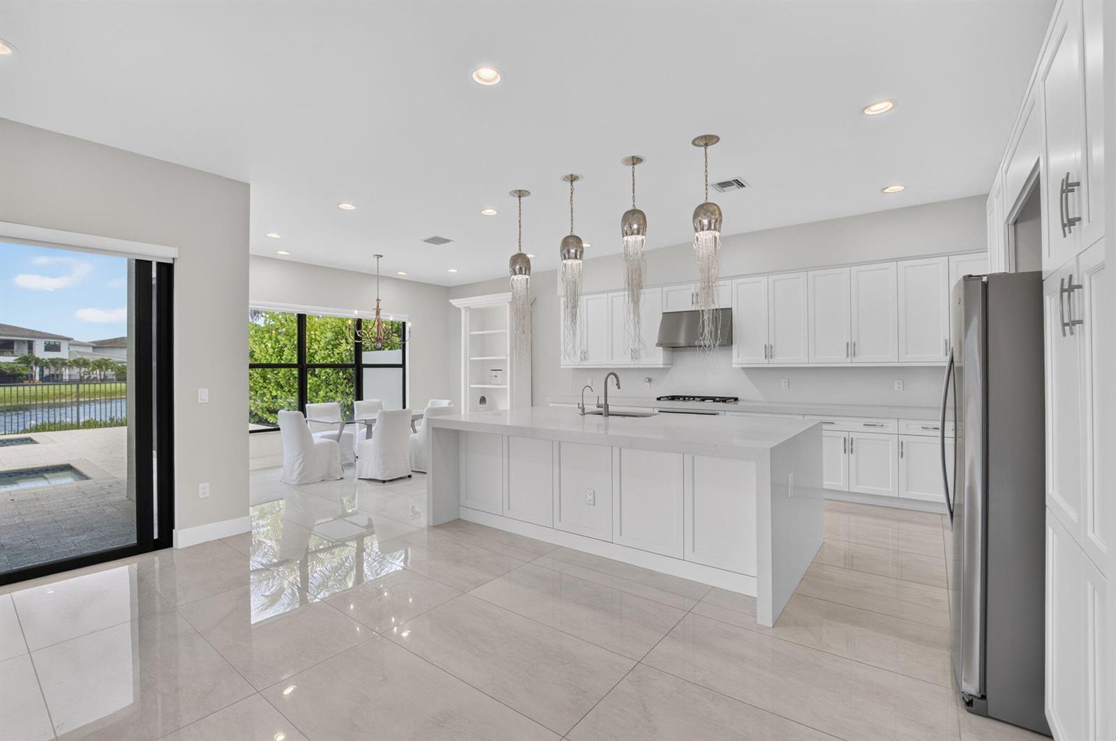 A modern white kitchen features a large island, pendant lighting, and a dining area nearby — 17100 Wandering Wave Avenue, Boca Raton FL 33496, BOCA RATON, FL