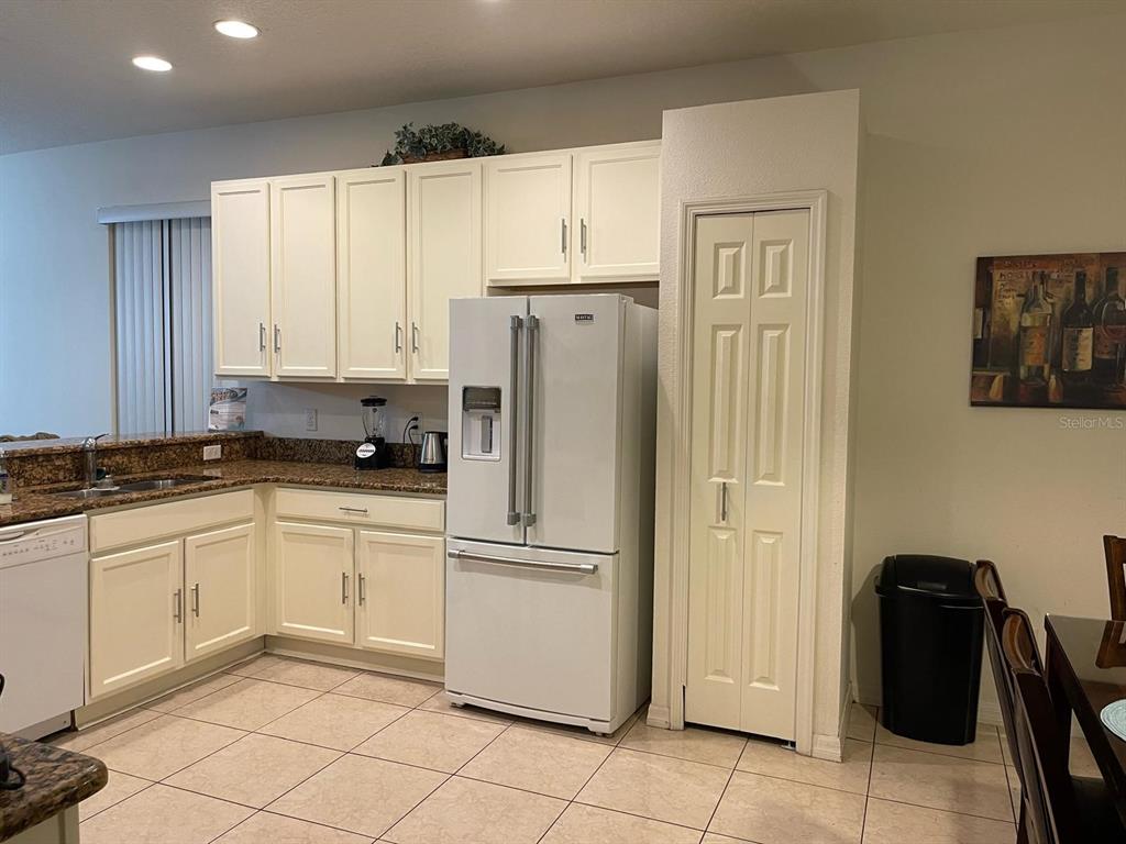 A kitchen features white cabinets, granite countertops, a white refrigerator, and a pantry closet — 1010 TOURMALINE DRIVE, KISSIMMEE, FL