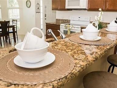 A kitchen island with granite countertops features place settings with white bowls and mugs — 1010 TOURMALINE DRIVE, KISSIMMEE, FL