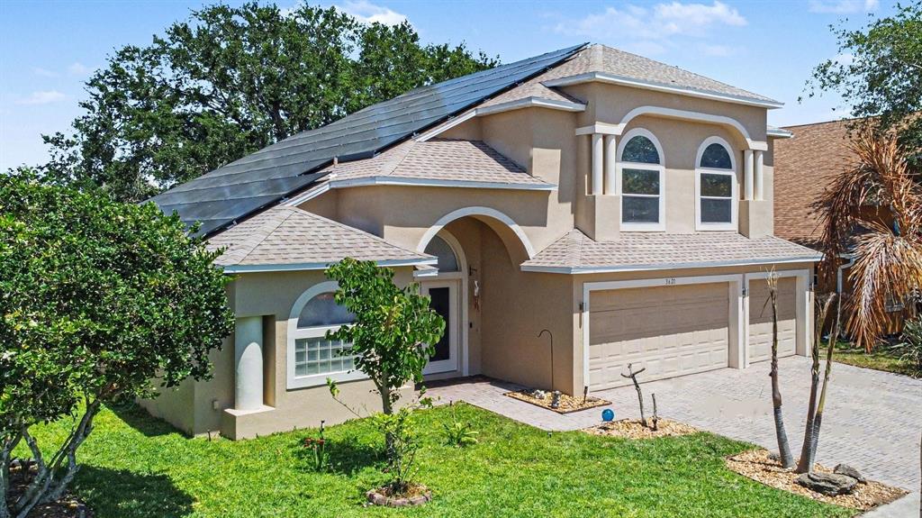A two-story tan house with a solar panel array on the roof and a garage — 3621 TIPPERARY DRIVE, MERRITT ISLAND, FL