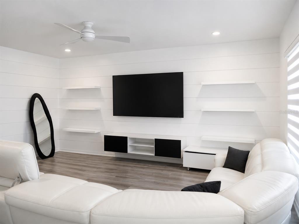 A modern living room features a white shiplap wall, floating shelves, and a white sectional sofa — 5225 TUSCANY LANE, DAVENPORT, FL