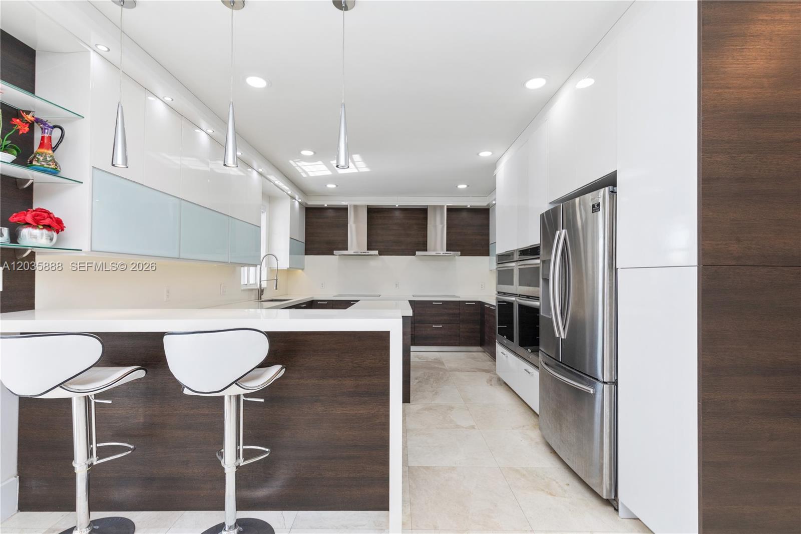 A modern kitchen features white glossy cabinets, dark wood accents, stainless steel appliances, and barstools — 2505 Hunters Run Way, Weston FL 33327, WESTON, FL
