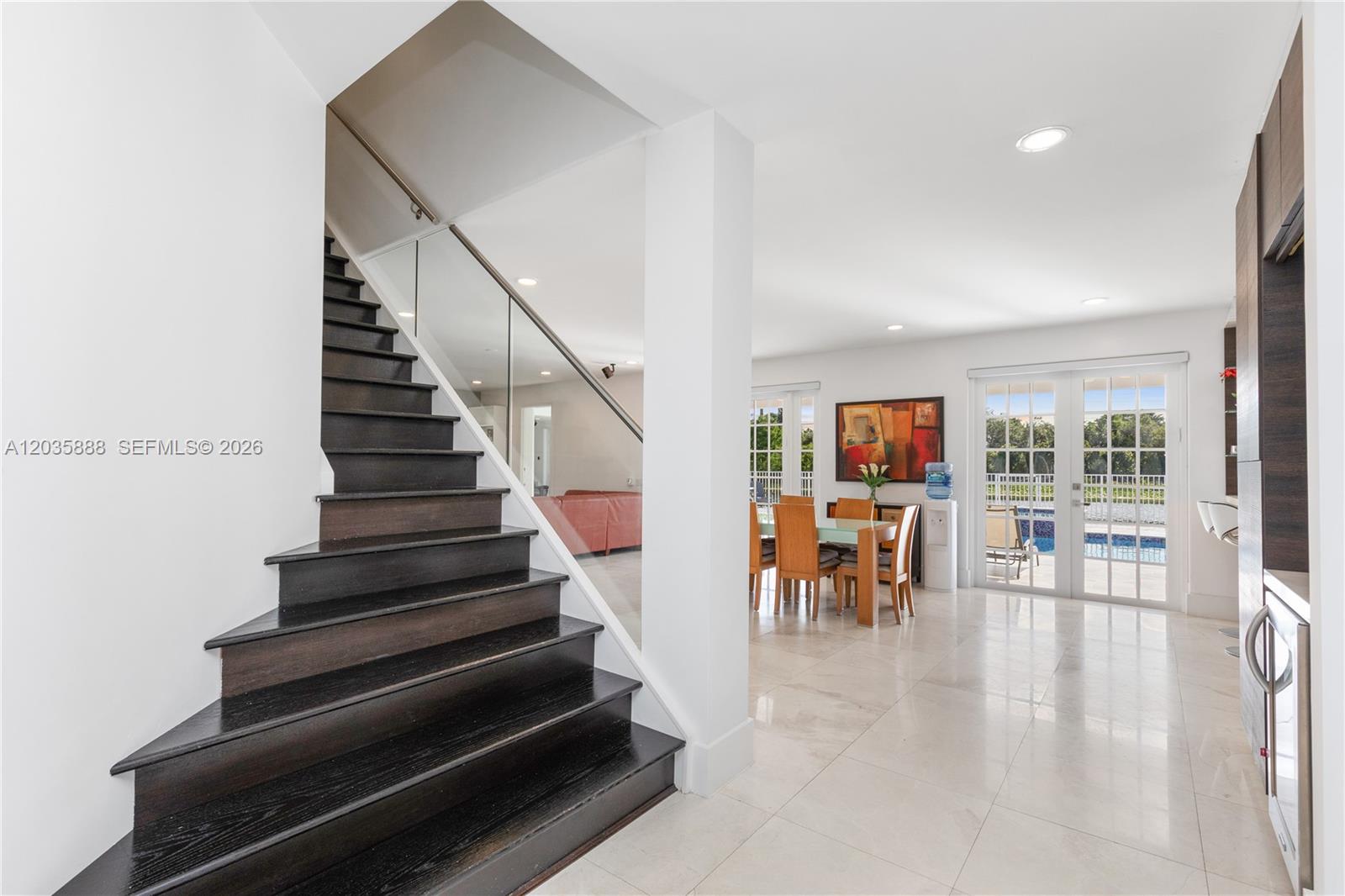 A staircase with dark wood treads leads to an open-concept dining area and patio doors — 2505 Hunters Run Way, Weston FL 33327, WESTON, FL