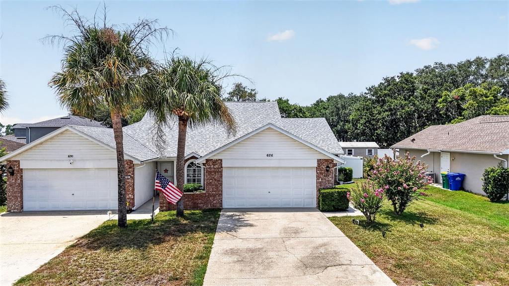 A single-story house with two garage doors, brick accents, and two palm trees in front — 626 WOODVIEW DRIVE, TAVARES, FL