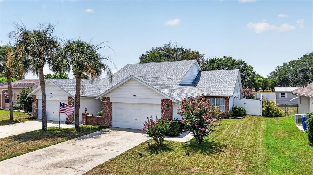 A single-story suburban house features a two-car garage, brick accents, and palm trees — 626 WOODVIEW DRIVE, TAVARES, FL