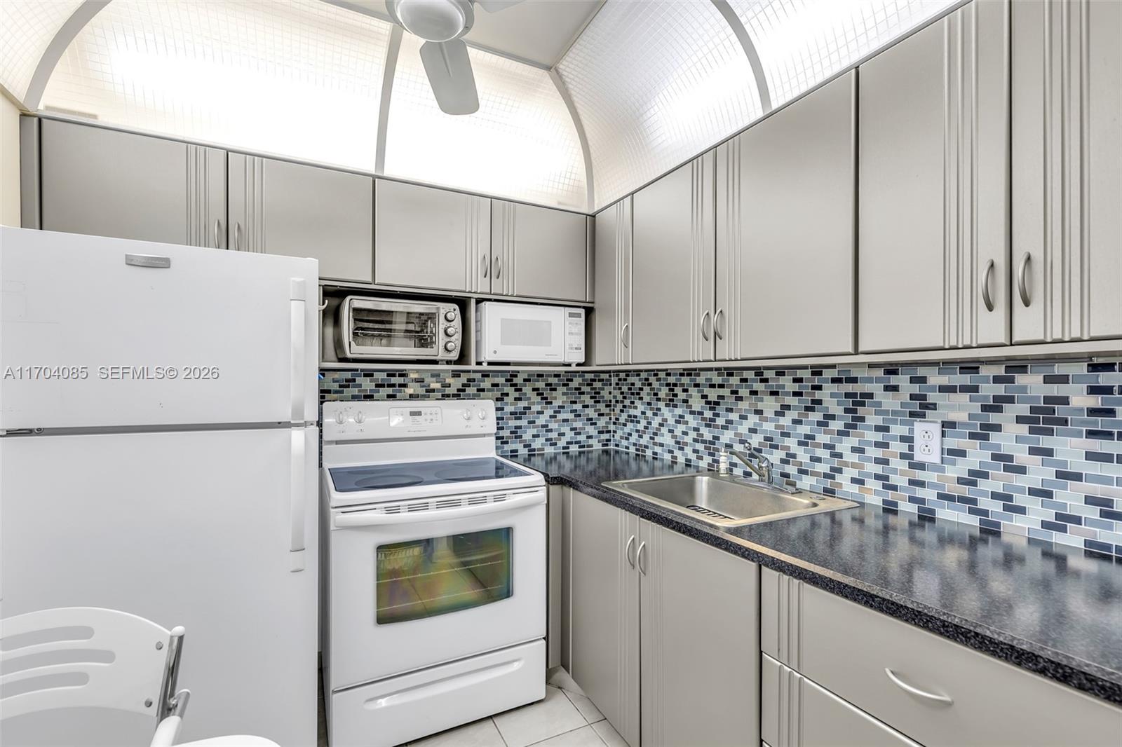 A kitchen features gray cabinets, a white stove, a white refrigerator, and a blue-tiled backsplash — 3029 Berkshire B # 3029, Deerfield Beach FL 33442, DEERFIELD BEACH, FL
