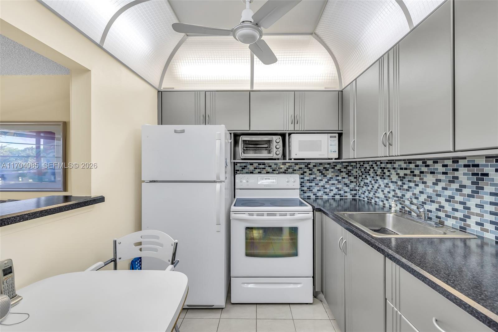 A kitchen features gray cabinets, white appliances, a mosaic tile backsplash, and a vaulted ceiling — 3029 Berkshire B # 3029, Deerfield Beach FL 33442, DEERFIELD BEACH, FL