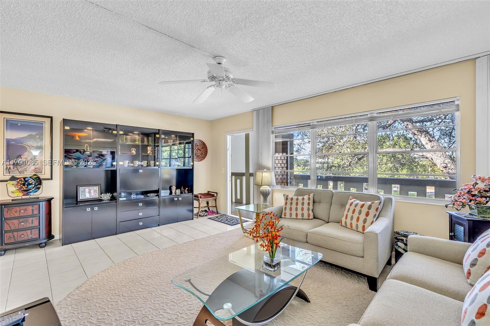 A living room features a beige sofa, glass coffee table, dark cabinetry, and large windows — 3029 Berkshire B # 3029, Deerfield Beach FL 33442, DEERFIELD BEACH, FL