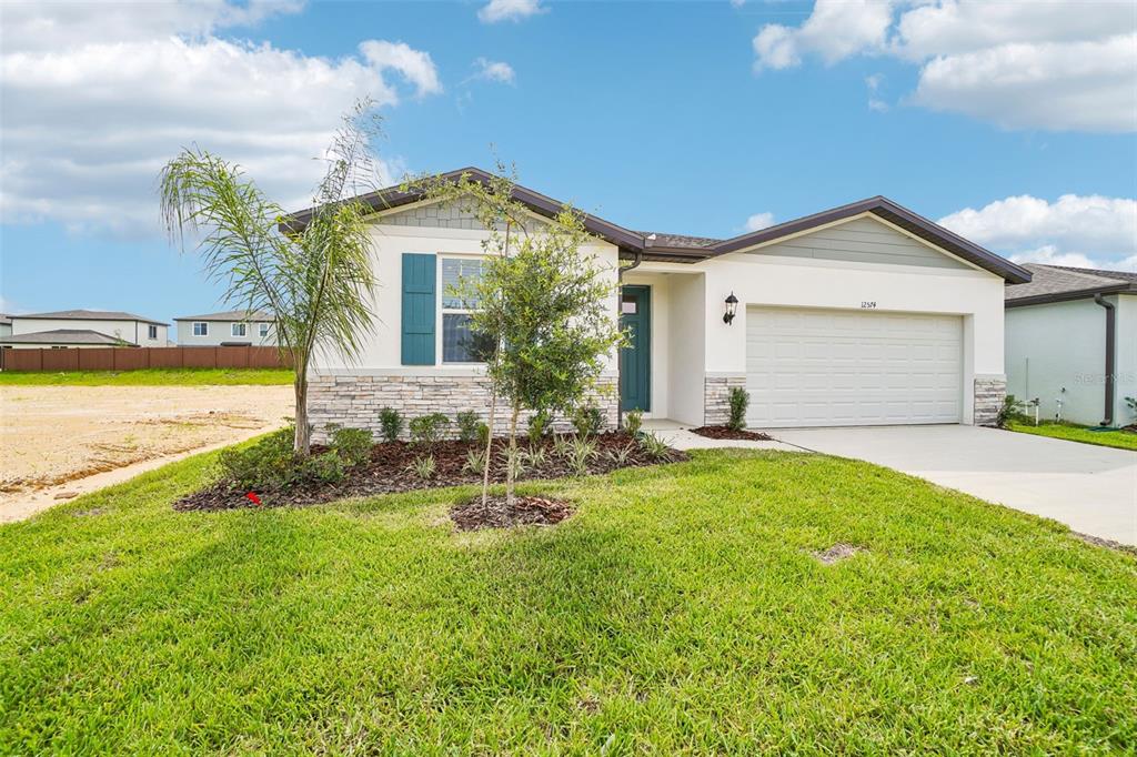 A single-story house with a two-car garage, stone veneer accents, and a front lawn — 12574 HOURGLASS WAY, DADE CITY, FL