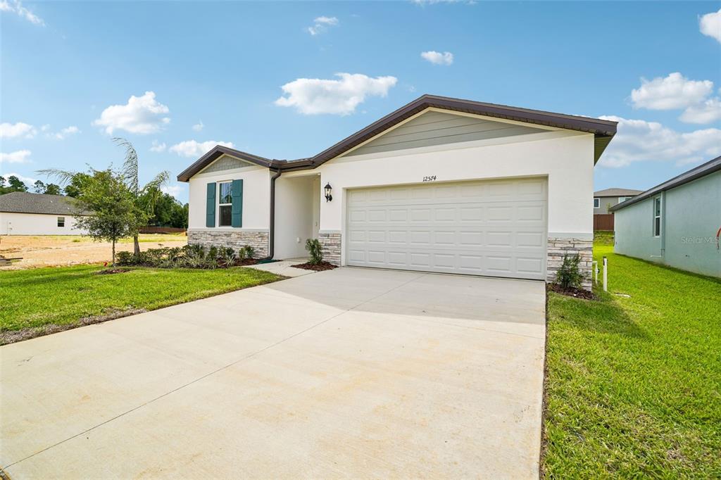 A single-story house with a white stucco exterior, stone accents, and a two-car garage — 12574 HOURGLASS WAY, DADE CITY, FL