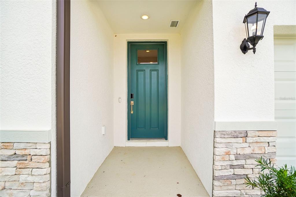 A teal front door is centered in a covered entryway with stone accents and stucco — 12574 HOURGLASS WAY, DADE CITY, FL