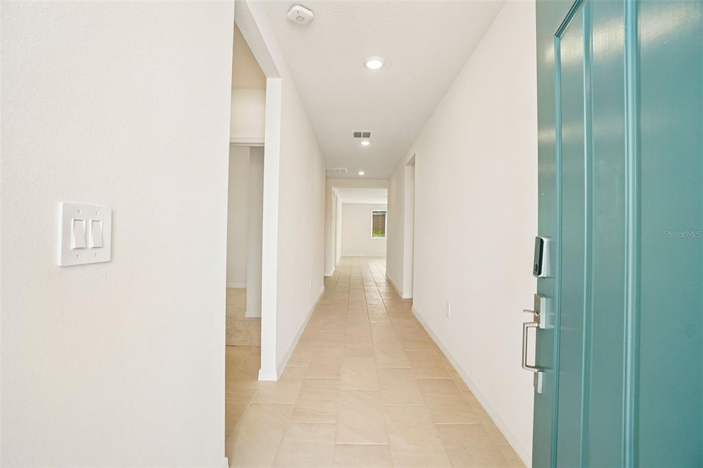 A view from an open teal door looking down a tiled hallway with recessed lighting — 12574 HOURGLASS WAY, DADE CITY, FL
