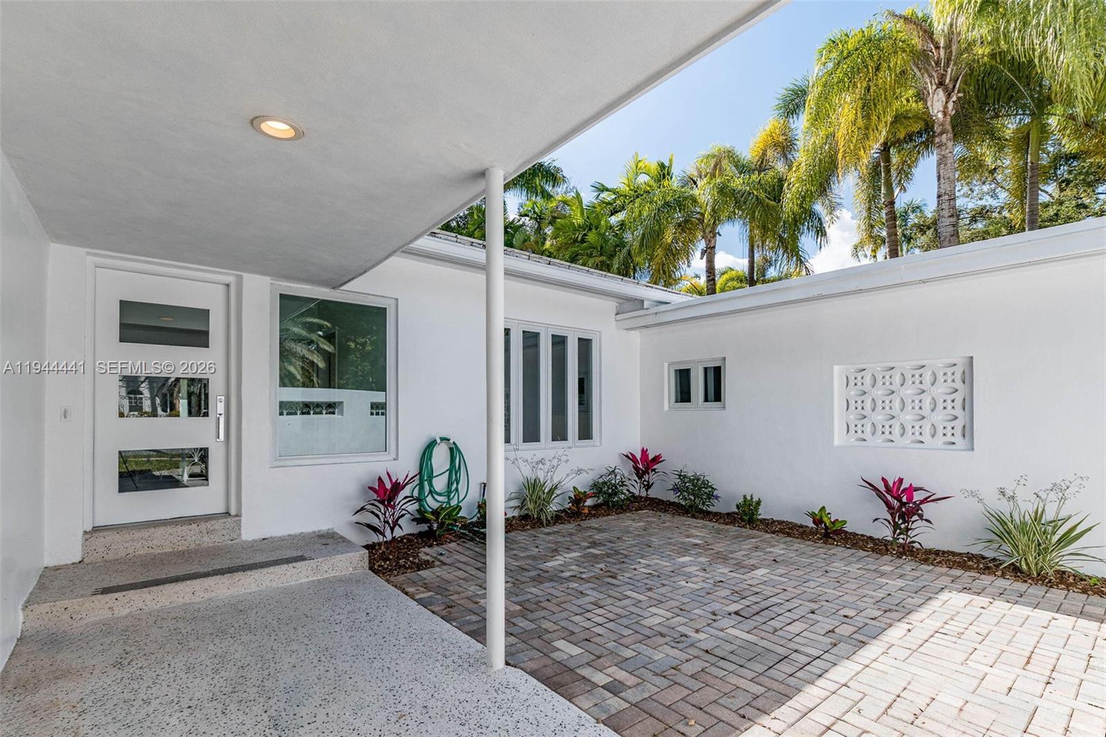 A white house exterior features a paved courtyard, a covered entryway, and tropical landscaping — 680 NE 57th St, Miami FL 33137, MIAMI, FL