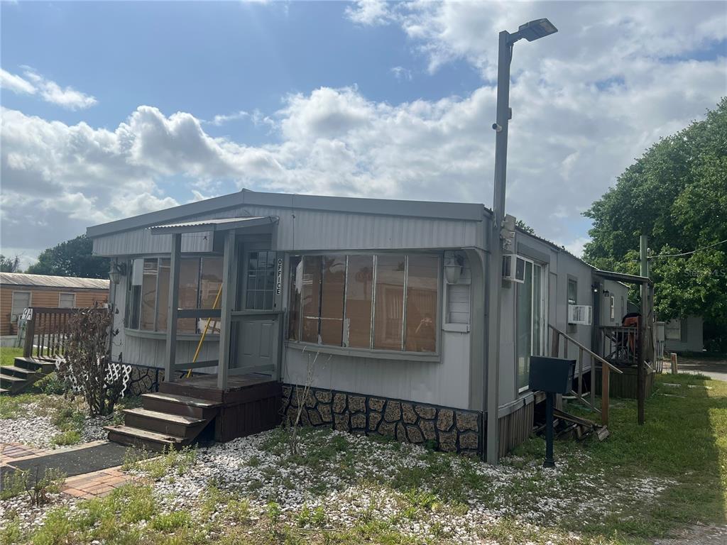 A single-story manufactured home with grey siding, a small front porch, and stone-patterned skirting — 15992 W COLONIAL DRIVE, OAKLAND, FL