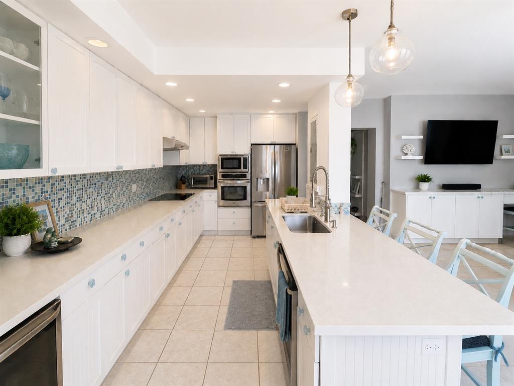 A white kitchen features a long island, stainless steel appliances, and a blue mosaic backsplash — 200 OCEAN DRIVE UNIT 231, HUMACAO, PR