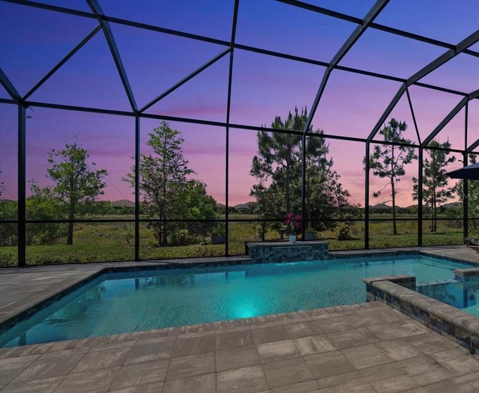 A screened-in swimming pool and spa overlook a grassy landscape at sunset — 729 TAILWIND PLACE, SARASOTA, FL