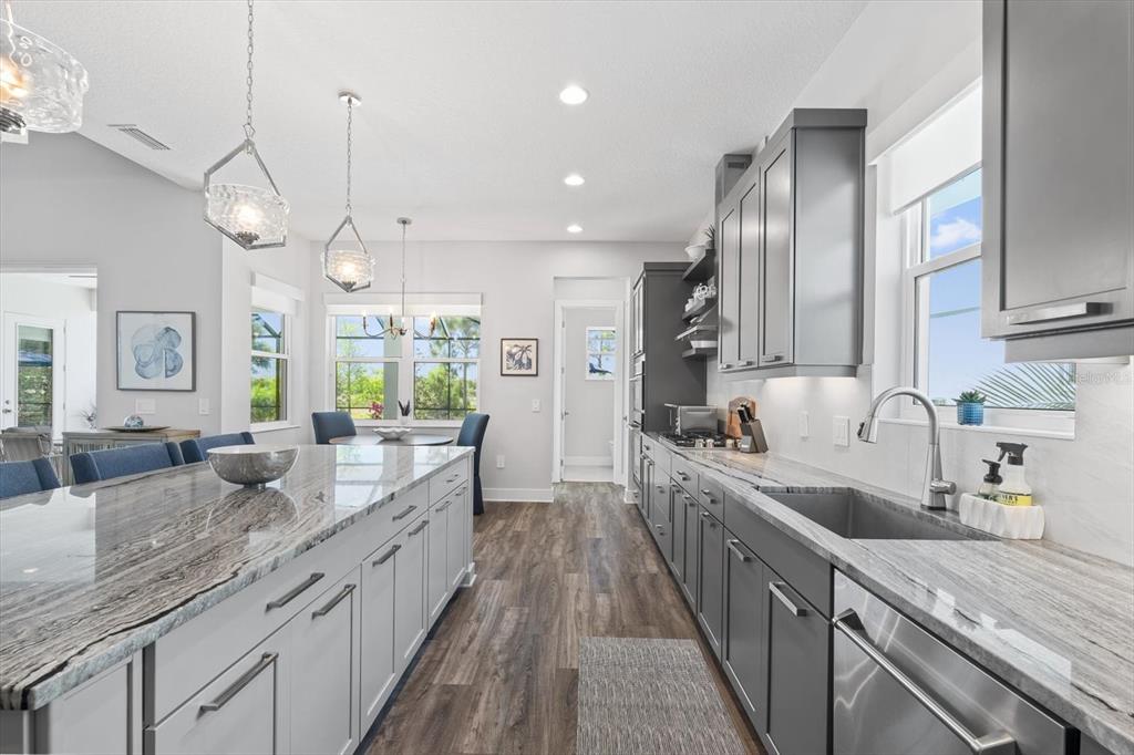 A modern kitchen features gray cabinets, stone countertops, a large island, and stainless steel appliances — 729 TAILWIND PLACE, SARASOTA, FL