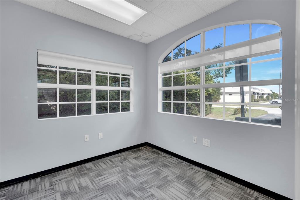 An empty office with gray walls, patterned carpet, and two large windows — 1825 COLONIAL BOULEVARD, FORT MYERS, FL