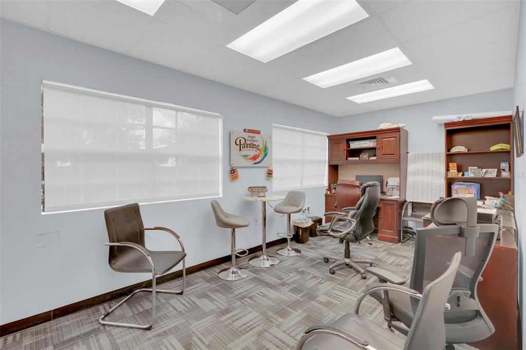 An office space features a desk, several chairs, a small table, and a wall sign — 1825 COLONIAL BOULEVARD, FORT MYERS, FL