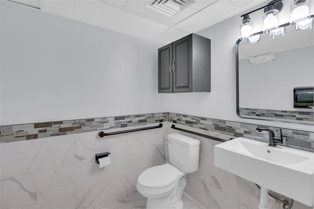 A bathroom features a wall-mounted sink, a toilet, grab bars, and gray cabinetry — 1825 COLONIAL BOULEVARD, FORT MYERS, FL