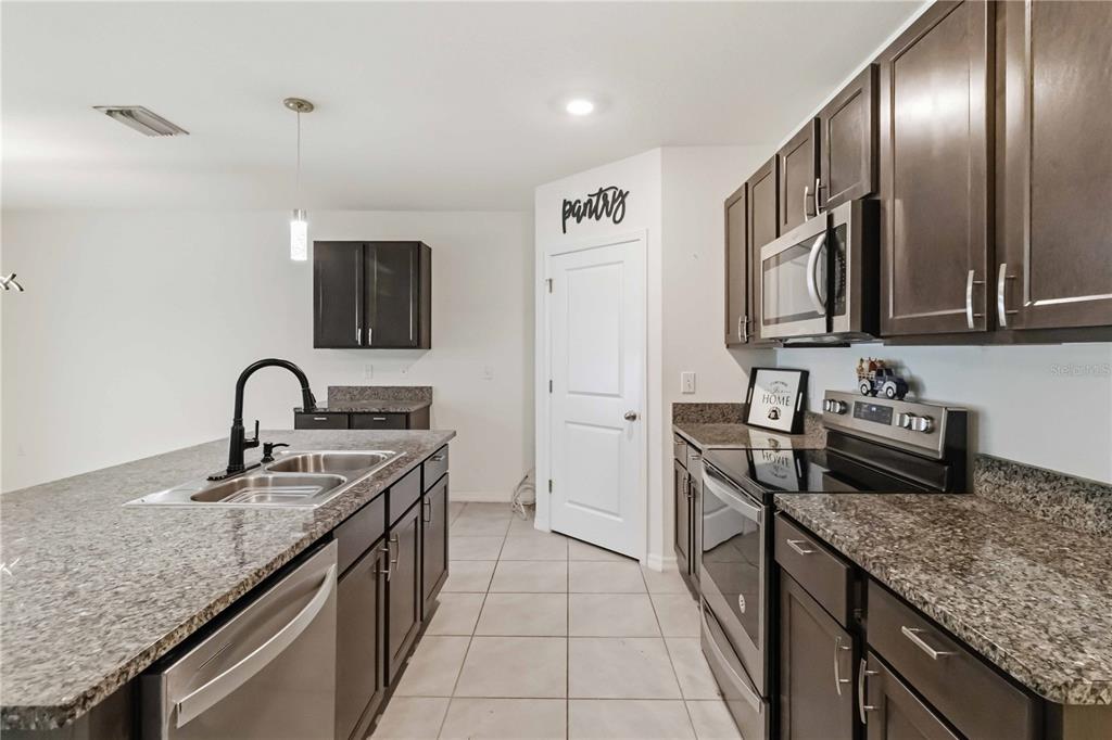 A kitchen features dark wood cabinets, granite countertops, a central island, and tile flooring — 1702 JOHNSON POINTE DRIVE, PLANT CITY, FL