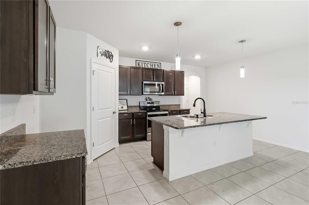 A kitchen with dark cabinets, granite countertops, and a stainless steel dishwasher faces a living area — 1702 JOHNSON POINTE DRIVE, PLANT CITY, FL