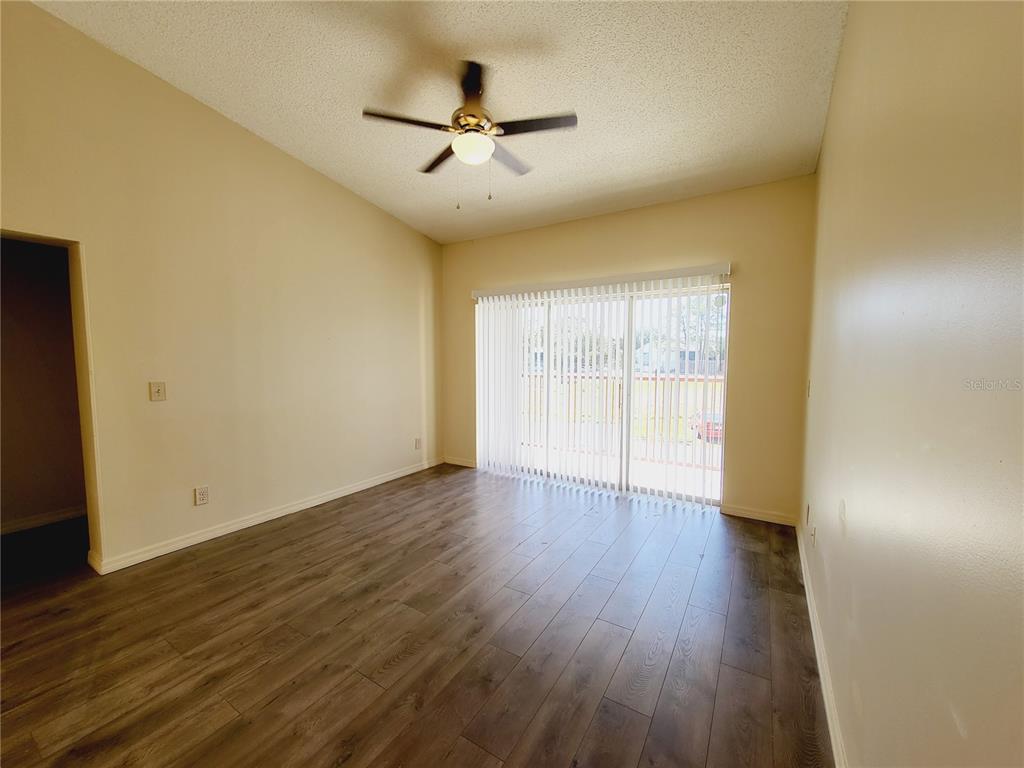 An empty room features wood-look flooring, a ceiling fan, and sliding glass doors with blinds — 4537 LAKEWAY DRIVE UNIT 3706, ORLANDO, FL