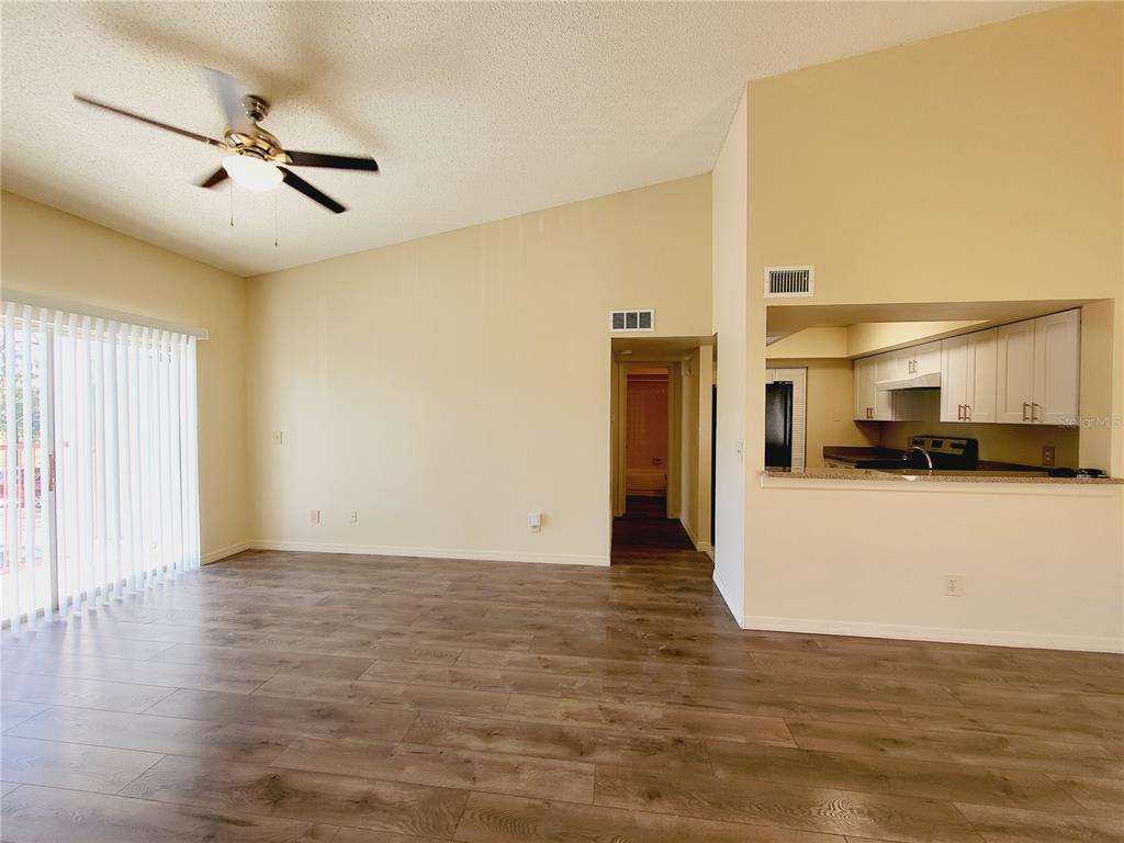 A living room with wood-look flooring, a ceiling fan, and an opening to the kitchen — 4537 LAKEWAY DRIVE UNIT 3706, ORLANDO, FL