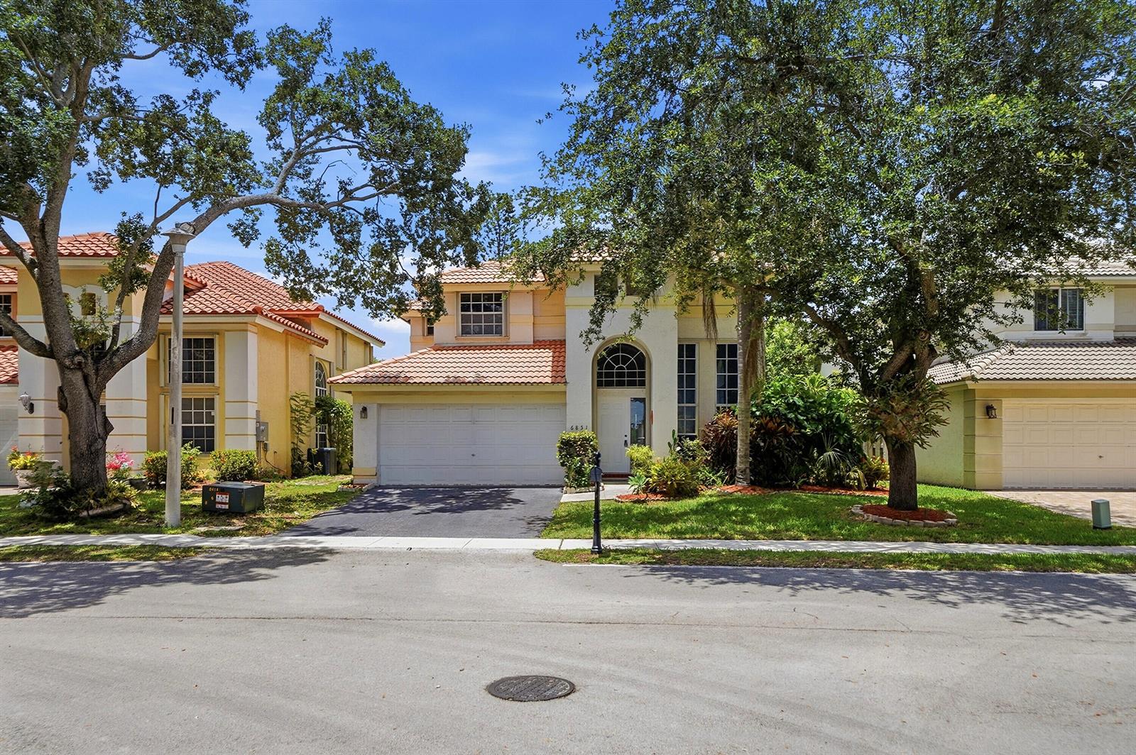A two-story suburban house with a tile roof, white garage, and large trees in front — 6851 NW 27th Street, Margate FL 33063, MARGATE, FL