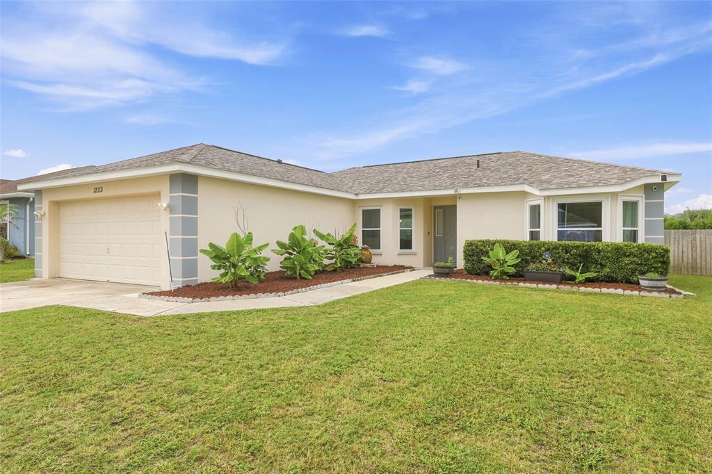 A single-story house with a beige stucco exterior, a two-car garage, and a front lawn — 1233 MERRIMACK DRIVE, DAVENPORT, FL