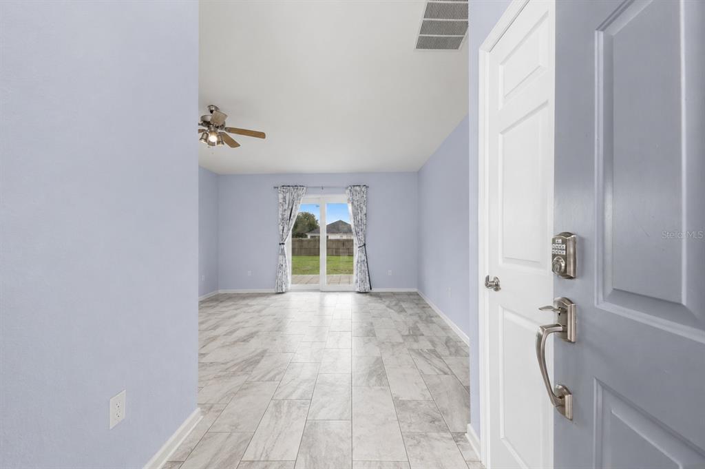 An entryway opens into a living room with light blue walls and gray tile flooring — 1233 MERRIMACK DRIVE, DAVENPORT, FL