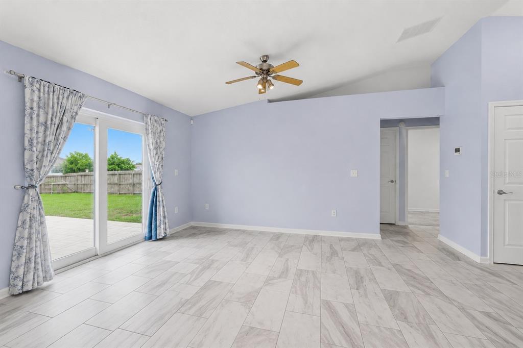 A living room with light blue walls, tile flooring, a ceiling fan, and sliding glass doors — 1233 MERRIMACK DRIVE, DAVENPORT, FL