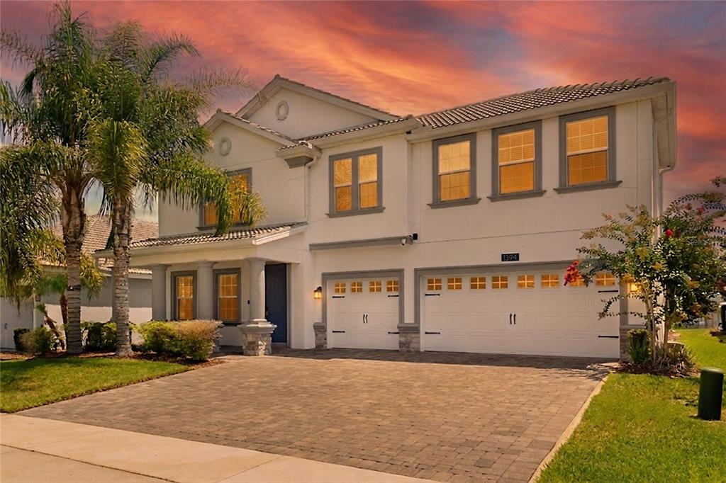 A two-story house with a paved driveway, three-car garage, and a palm tree at sunset — 1394 OLYMPIC CLUB BOULEVARD, CHAMPIONS GATE, FL