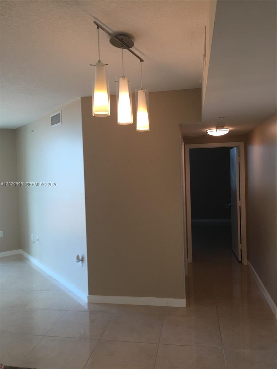 A hallway leads to a dark room, featuring a three-light pendant fixture and tile flooring — 9066 SW 73rd Ct # 907, Miami FL 33156, MIAMI, FL