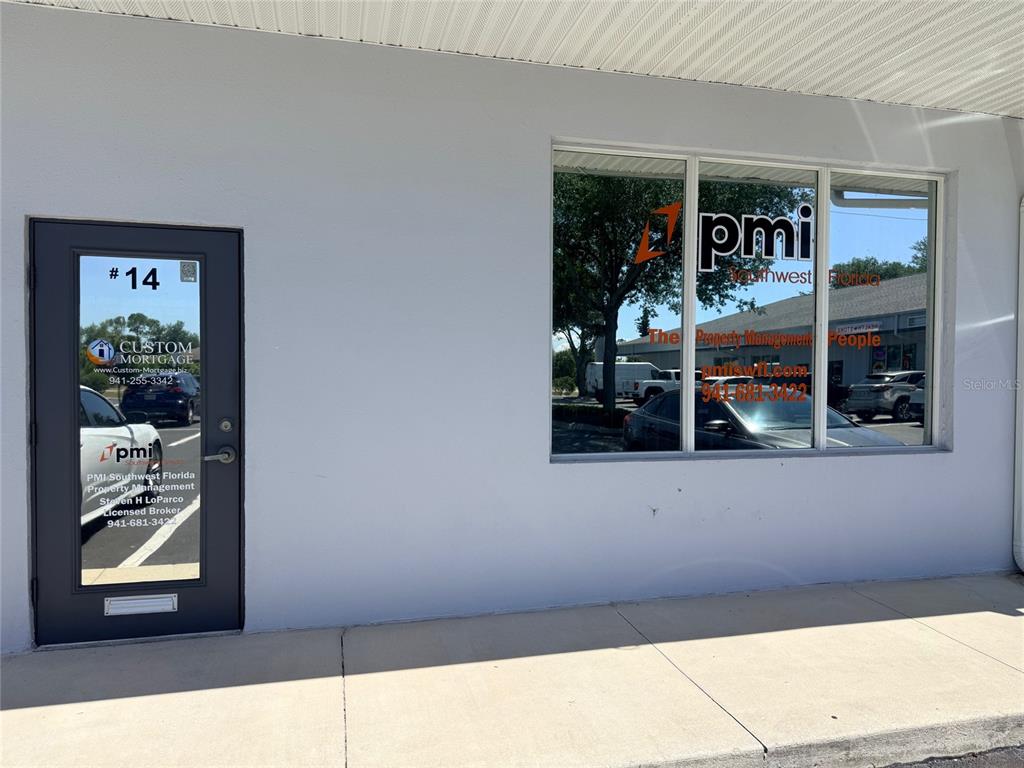 The exterior of a commercial office unit features a dark door and large glass windows — 20020 VETERANS BOULEVARD UNIT 14, PORT CHARLOTTE, FL