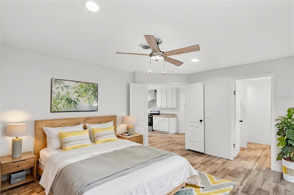 A bedroom with light wood flooring, a ceiling fan, and an open doorway to a kitchen — 17475 TAVERN ROAD, BROOKSVILLE, FL